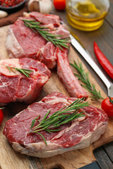 Pieces of raw beef and rosemary on wooden table, closeup