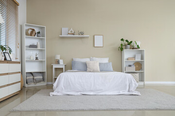 Stylish interior on bedroom with comfortable bed, chest of drawers and shelving units