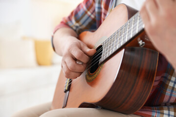Fototapeta premium Man playing guitar at home, focus on hand