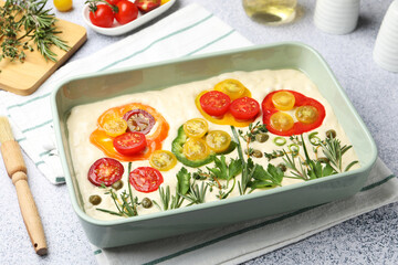 Raw focaccia with vegetables, spices and brush on light grey table, closeup