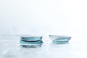 Pair of contact lenses and water drops on white mirror surface, closeup