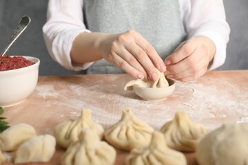Woman making khinkali on table in kitchen, closeup