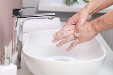 Woman washing her hands with foaming soap above sink in bathroom, closeup