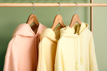 Rack with stylish hoodies on green background, closeup