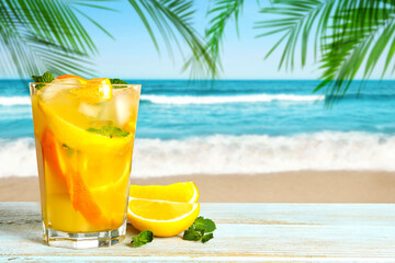 Refreshing cocktail on wooden deck under green palm leaves on tropical beach
