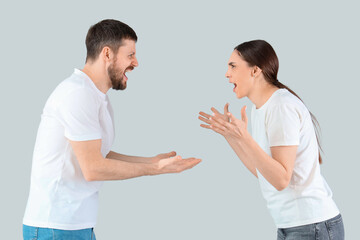 Angry young couple quarreling on light background