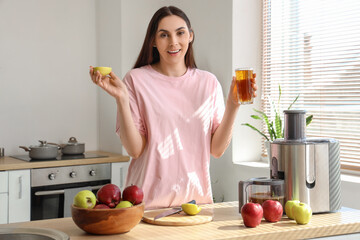 Young woman with fresh apple juice and modern juicer at table in kitchen