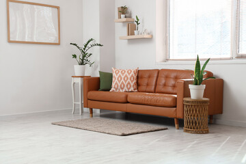 Interior of light living room with brown sofa, plants and blank frame