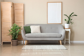 Interior of light living room with grey sofa, blank frame and folding screen