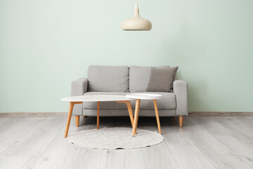 Sofa with coffee tables, rug and chandelier near grey wall in living room