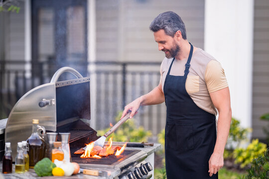 Middle aged man preparing barbecue grill outdoor. Man cooking barbecue grill at backyard. Chef preparing food on barbecue. Millennial man grilling meat on barbecue grill. Bbq party. Meal grilling.