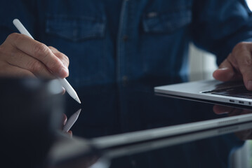 Close up of business man using stylus pen signing e-document on digital tablet via mobile app, working on laptop computer on office, e-signing, proofing document