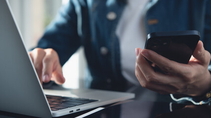 Closeup, business woman using smartphone during working on laptop at home office. Young asian woman freelancer surfing the internet, online working from home