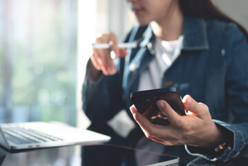 Closeup, young asian business woman working on laptop computer and using mobile phone at home office. Student studying online class, searching the information and surfing the internet, e-learning