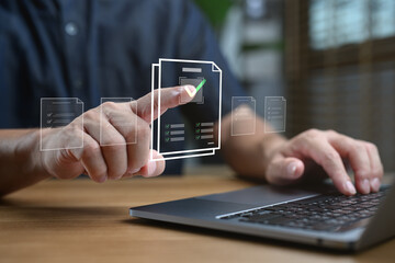 Hand touching digital document on virtual interface, approving checklist on laptop computer, concept of paperless office, online form, digital workflow and business technology.