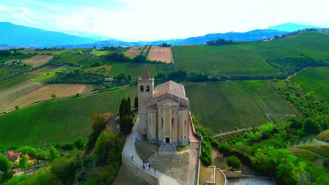 OFFIDA, ITALY - AUGUST 4, 2024: Aerial fly-over push-in shot of Chiesa di Santa Maria della Rocca. Elevated view of the church on a rocky promontory, with walls, Gothic details and lush valley views