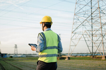 Asian male engineers are working under the power transmission tower.