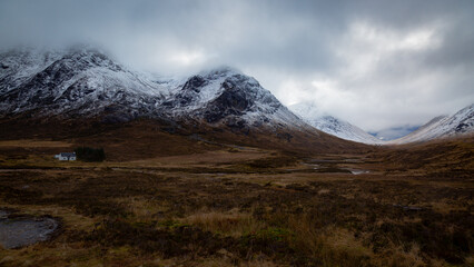 A breathtaking panoramic view of the Scottish Highlands, featuring snow-capped mountains rising above vast open moorland and rugged terrain.