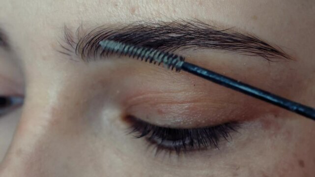 Eyebrow lining with cosmetic brush and eyebrow mascara. Close-up macro video of beautiful female face make up.