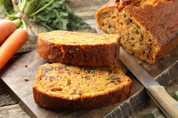 Homemade carrot cake with nuts, knife and vegetables on wooden table, closeup