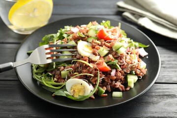 Delicious salad with brown rice on black wooden table, closeup