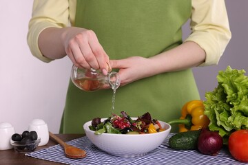 Woman pouring oil onto tasty salad at wooden table against white background, closeup