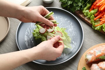 Woman making tasty spring roll at grey wooden table, closeup