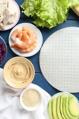 Rice paper sheets and different ingredients on blue wooden table, flat lay