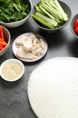 Rice paper sheets and different ingredients on dark grey table, above view
