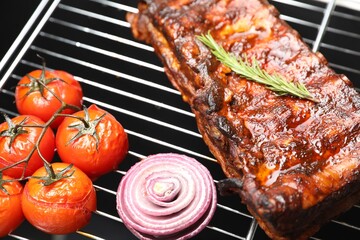 Delicious roasted pork ribs with rosemary, onion and tomatoes on grill, closeup