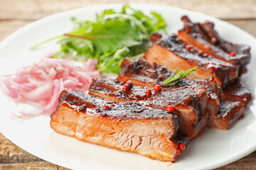 Delicious spare ribs, onion and arugula on wooden table, closeup