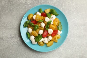 Tasty salad with yellow tomatoes, basil and mozzarella cheese on light grey table, top view