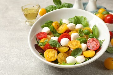Tasty salad with yellow tomatoes, basil and mozzarella cheese on light grey table, closeup
