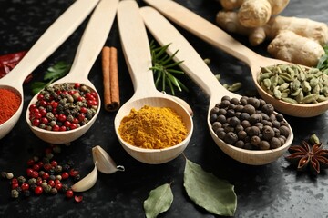 Many different spices in spoons on black table, closeup