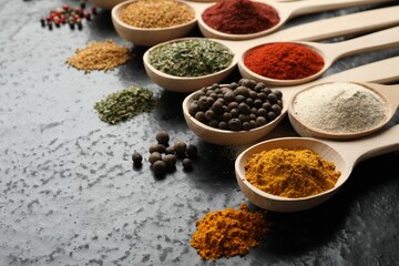Many different spices in spoons on black table, closeup