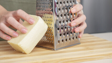 chef grating traditional parmesan cheese with steel grater on the wooden board
