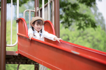 新緑の公園で滑り台で遊ぶ幼児　公園のお出かけやレジャーのイメージ