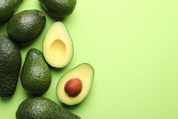 Whole and cut avocados on light green background, flat lay. Space for text