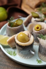 Delicious herring rolls with olives, pickles and dill on table, closeup