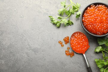 Tasty red caviar in bowl, spoon and parsley on grey table, flat lay. Space for text