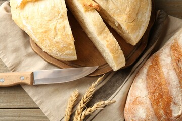 Cut freshly baked bread, spikes and knife on wooden table, flat lay
