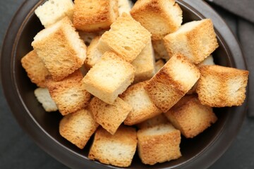 Tasty crispy croutons in bowl on dark textured table, top view