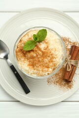 Delicious rice pudding with cinnamon, mint and spoon on white wooden table, top view