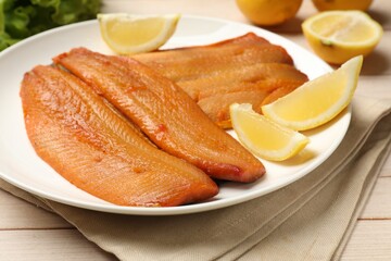 Delicious smoked herring fillets with lemon slices on white wooden table, closeup