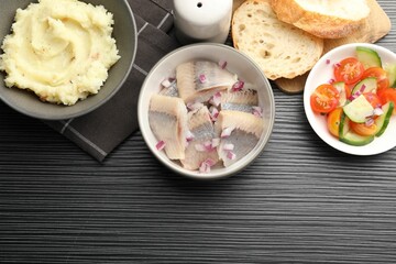 Delicious herring pieces with onions served on black wooden table, flat lay