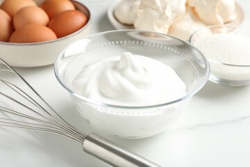 Whisk, whipped cream in bowl and other ingredients on light table, closeup. Cooking meringue cookies