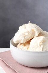 Delicious homemade meringue cookies in bowl on table against gray background, closeup