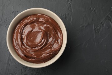 Tasty chocolate pudding in bowl on black table, top view. Space for text