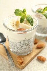 Delicious dessert with chia seeds, yogurt, banana, almond and mint in glasses on light textured table, closeup. Superfood