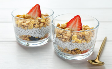 Delicious dessert with chia seeds, yogurt, granola and strawberries in glasses on white wooden table, closeup. Superfood